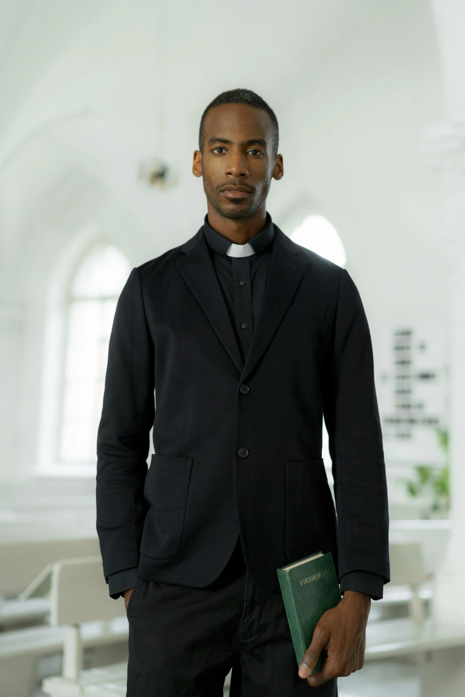 a man standing in a room holding a book, holy themed, black jacket, avant uniform, black man