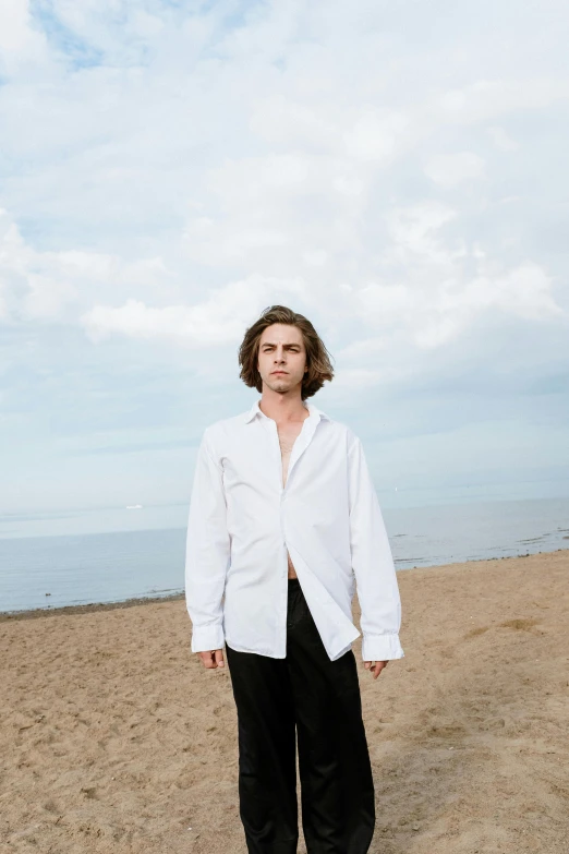 a man standing on top of a sandy beach, an album cover, inspired by Daniël Mijtens, renaissance, wearing a white button up shirt, timothee chalamet, high resolution image, concert photo