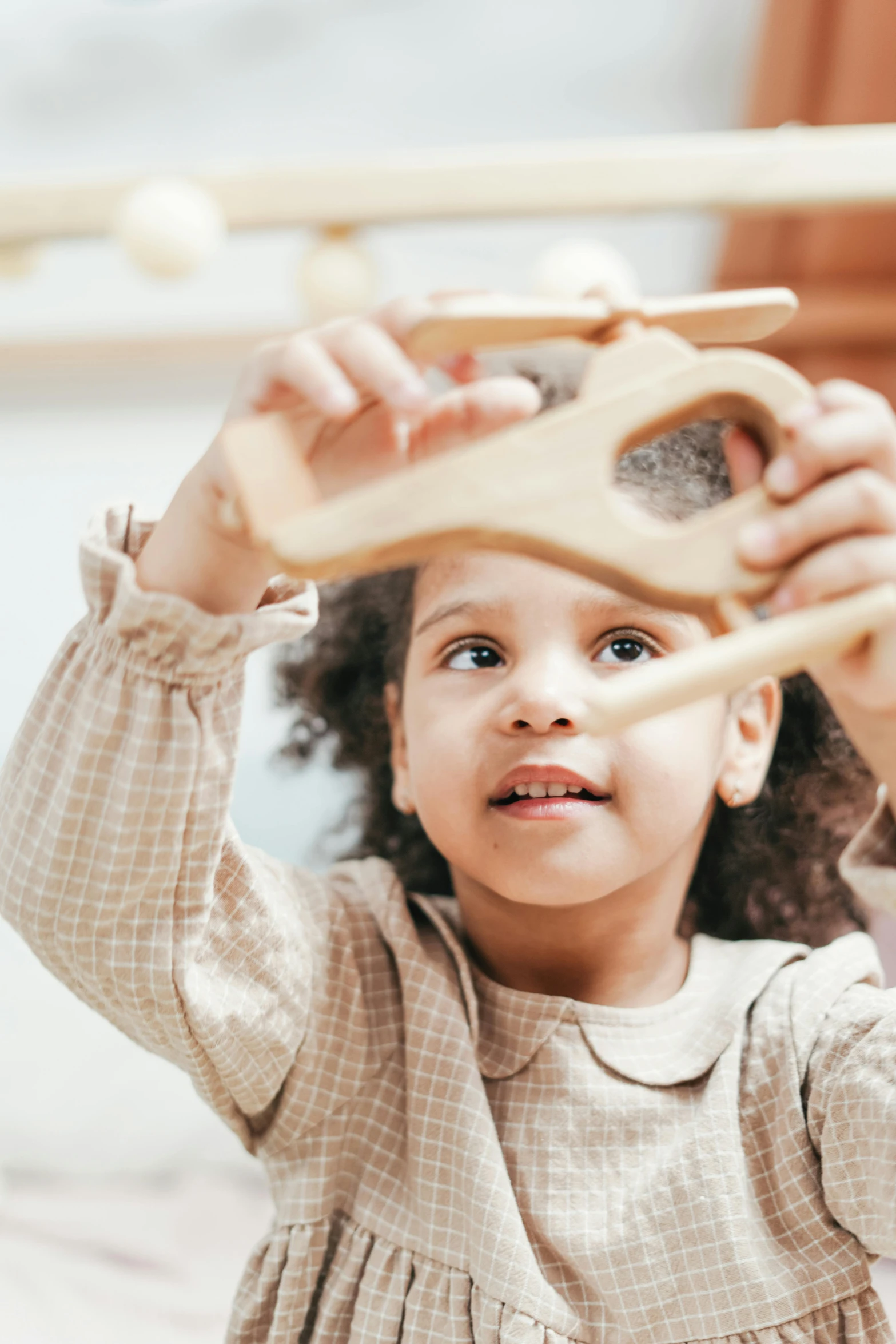 a little girl playing with a wooden toy, pexels contest winner, light skinned african young girl, organic shapes, holding it out to the camera, pictured from the shoulders up