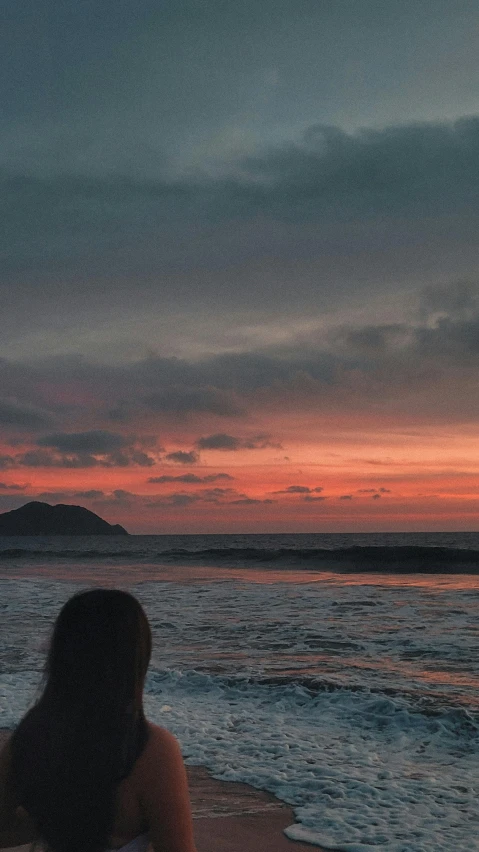 a woman standing on top of a beach next to the ocean, a picture, unsplash contest winner, sumatraism, ((sunset)), facing away, tsunami behind him, red hues