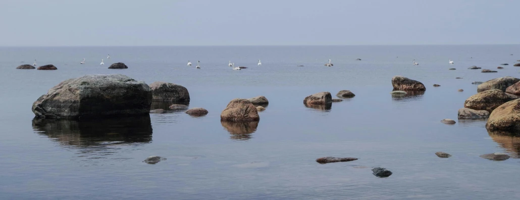 a number of rocks in a body of water, a picture, by Jaakko Mattila, unsplash, romanticism, birds in the distance, ignant, summer day, 2022 photograph