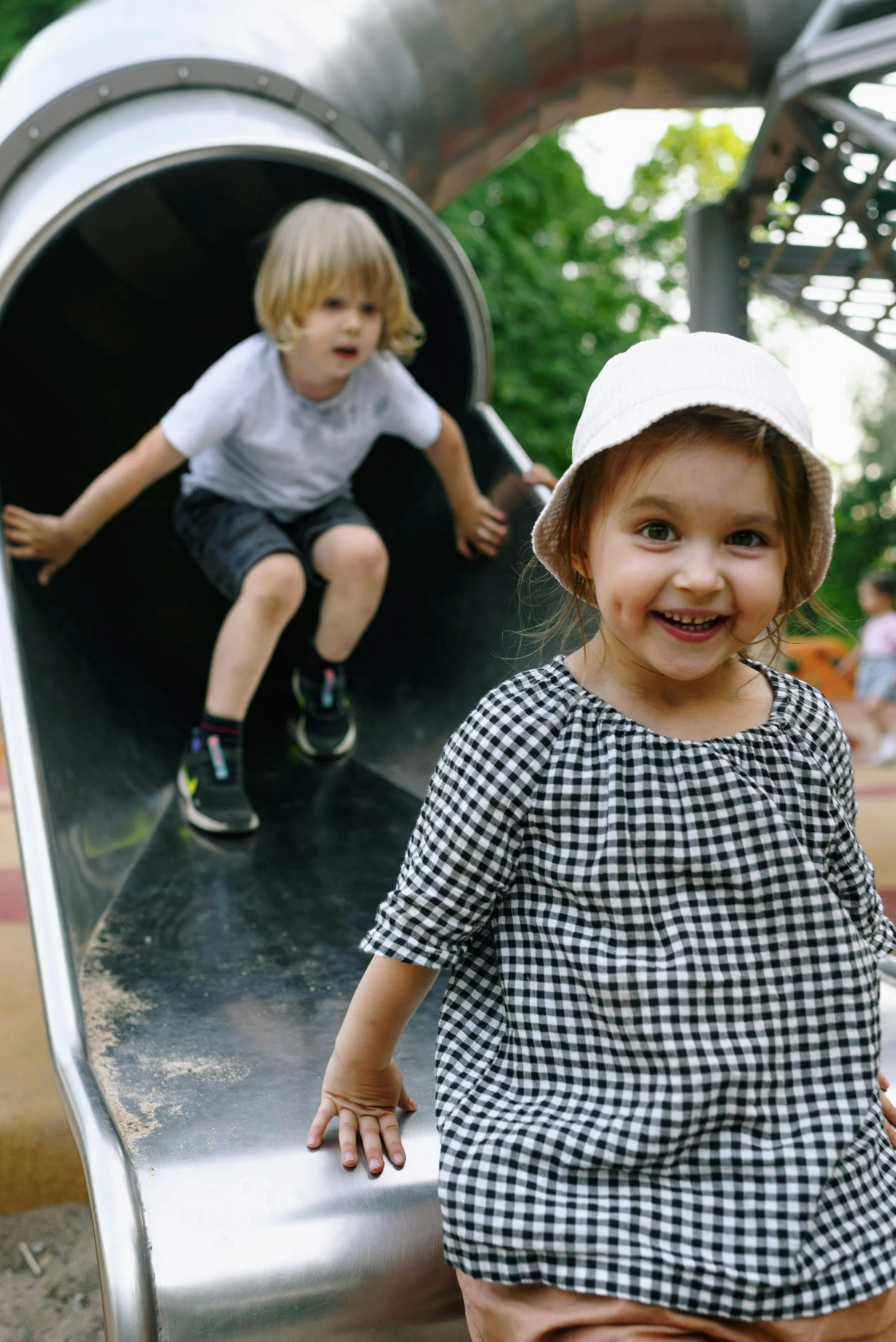 a little girl sitting on top of a slide, pexels contest winner, boy and girl, park in background, grey, smiling down from above