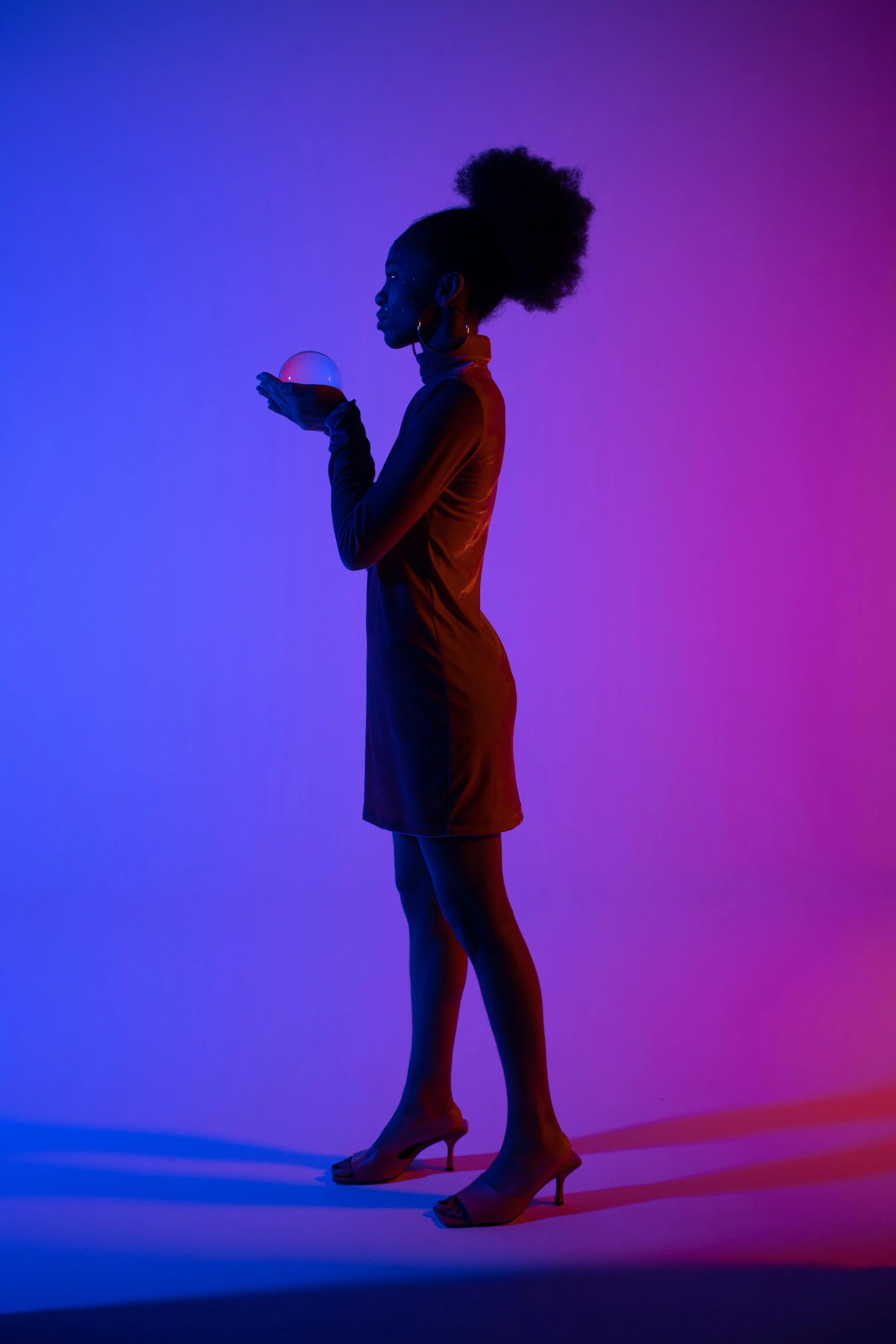 a woman standing in front of a purple and blue background, inspired by Carrie Mae Weems, pexels contest winner, colored gel lighting, holding a glowing orb, full body profile pose, ( ( dark skin ) )