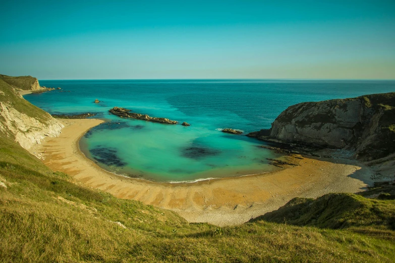 a large body of water sitting on top of a lush green hillside, by Peter Churcher, pexels contest winner, victorian arcs of sand, cyan and orange, chalk cliffs above, vintage glow