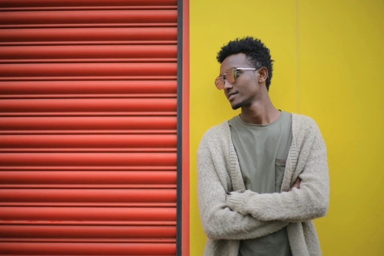 a man standing in front of a red garage door, inspired by Afewerk Tekle, pexels contest winner, afrofuturism, yellows and reddish black, androgynous person, ethiopian, casually dressed