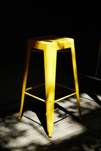 a yellow stool sitting on top of a wooden floor, a portrait, unsplash, dappled sunlight, 155 cm tall, metalwork, back - lit