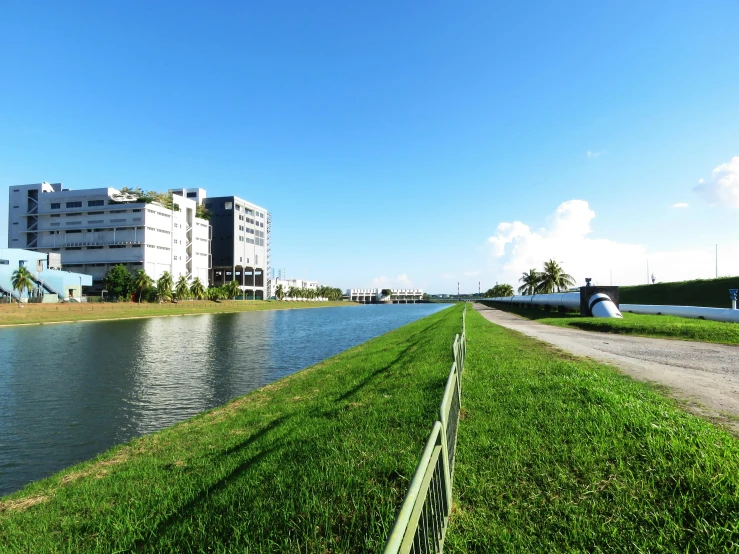 a large body of water sitting next to a lush green field, inspired by Tadao Ando, singapore esplanade, vice city, medical research facility, railing along the canal