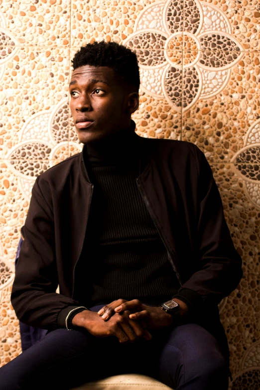 a man sitting on a stool in front of a wall, an album cover, by Emanuel Witz, trending on unsplash, renaissance, adut akech, black turtle neck shirt, profile image, looking off to the side