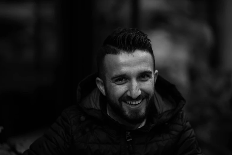 a black and white photo of a man smiling, by Adam Marczyński, hurufiyya, dressed in leather jacket, edin durmisevic, professional profile picture, complex background