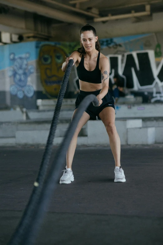 a woman holding a rope in a parking lot, she is wearing a black tank top, working out, gif, asher duran