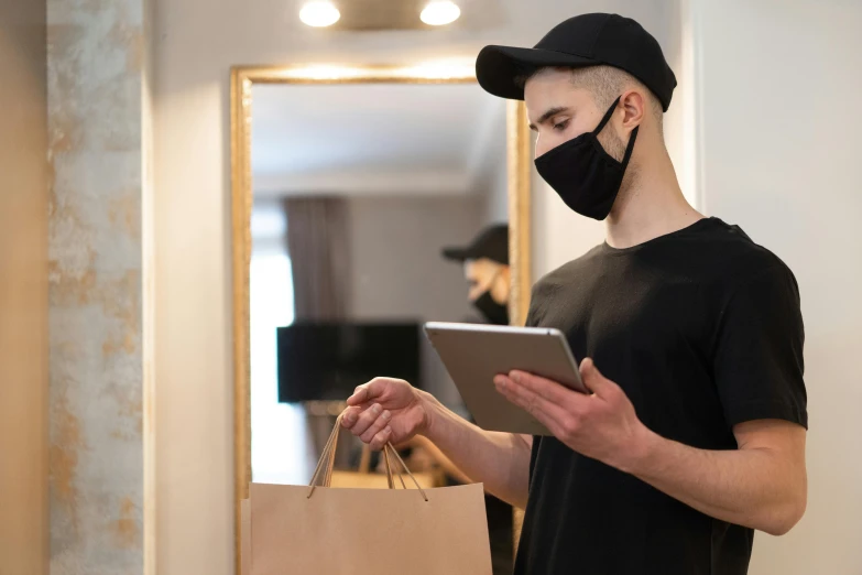 a man wearing a face mask while looking at a tablet, by Joseph Severn, delivering packages for amazon, round mirror on the wall, wearing a black tshirt, face covered