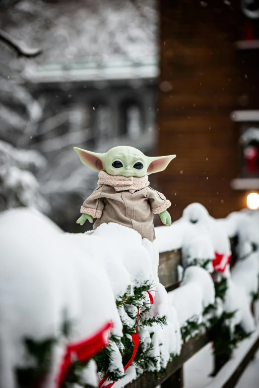 a toy is sitting on a fence in the snow, inspired by George Lucas, unsplash, giant yoda, decorations, avatar image, switzerland