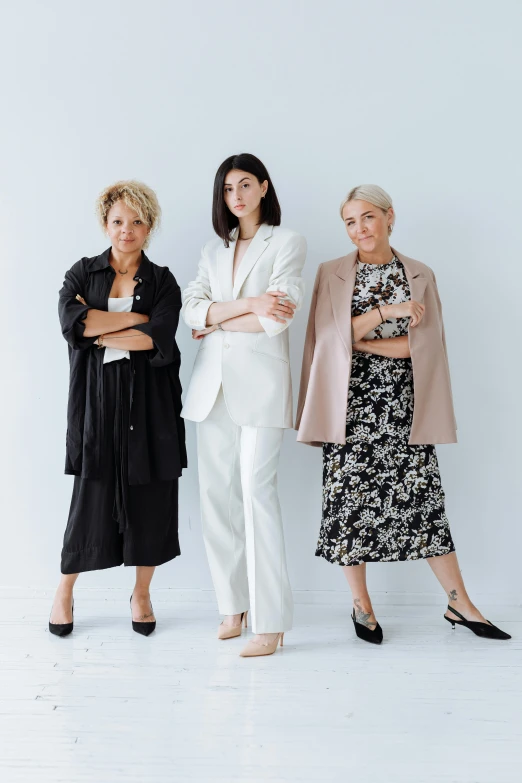 three women standing in front of a white wall, a portrait, unsplash, trench coat and suit, confident stance, ivy's, maternal