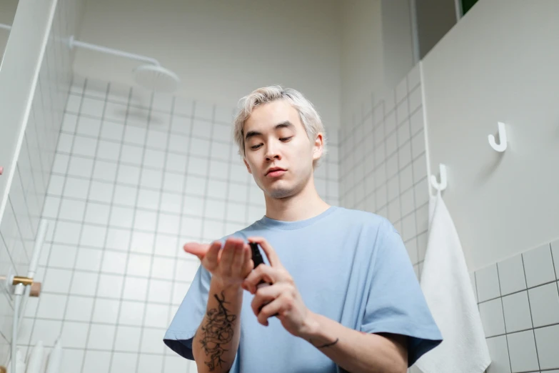 a man standing in a bathroom looking at his cell phone, a tattoo, trending on pexels, pale hair, loish and ross tran, performing, with index finger