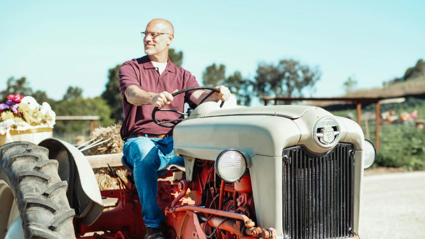 a man sitting on top of a red tractor, a portrait, pexels, bald man, california;, avatar image, ad image