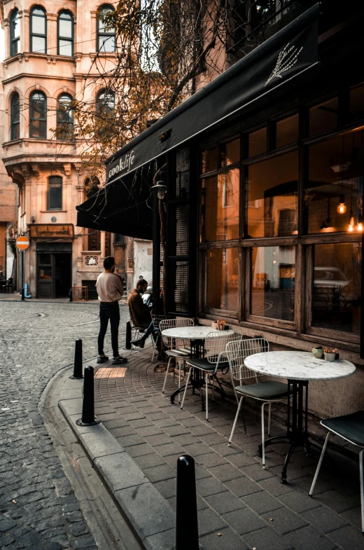 a couple of people walking down a cobblestone street, by Cafer Bater, pexels contest winner, art nouveau, cafe tables, turkey, man sitting facing away, inspect in inventory image