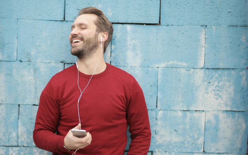 a man standing in front of a blue wall listening to music, trending on pexels, red sweater and gray pants, smiling slightly, aura jared and wires, man in his 40s