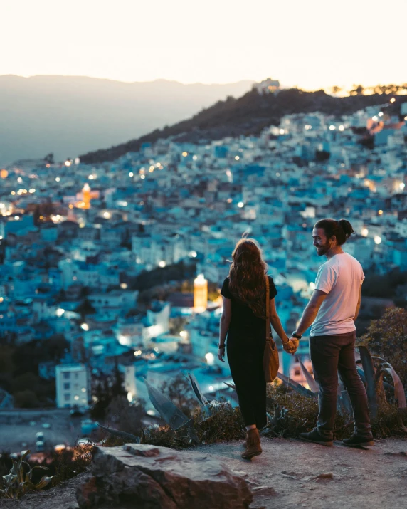 a man and a woman standing on top of a hill, trending on unsplash, happening, moroccan city, so cute, blue, bright city lights