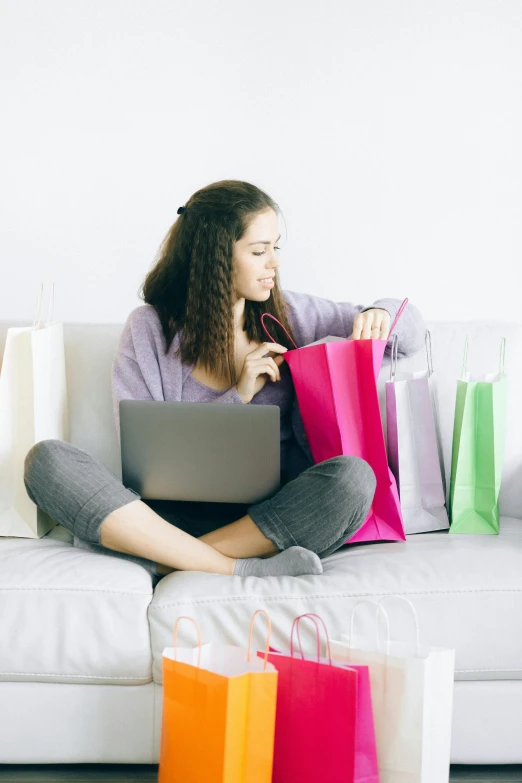 a woman sitting on a couch with shopping bags and a laptop, square, premium, multi - coloured, small