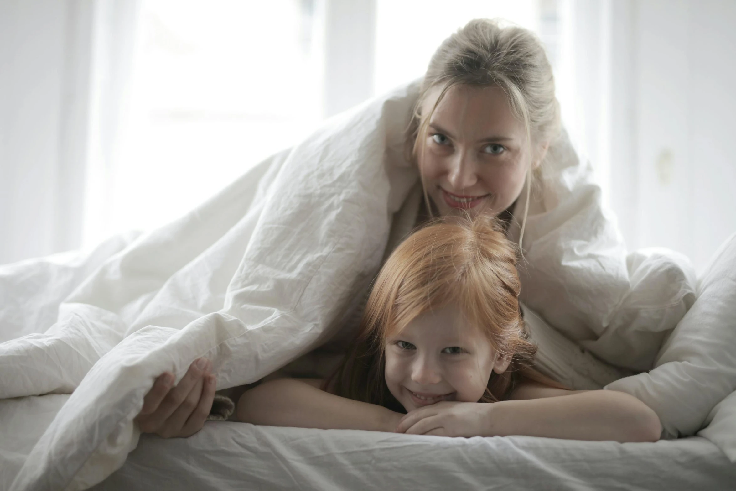 a woman and a child under a blanket on a bed, pexels contest winner, redhead girl, thumbnail, white, linen