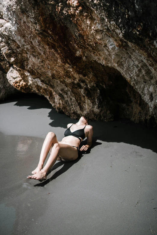 a woman laying on a beach next to a rock, unsplash, black underwear, with pale skin, devastated, caves