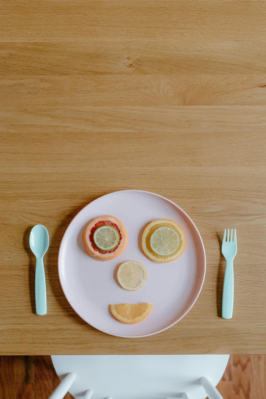 a pink plate sitting on top of a wooden table, unsplash, silly playful fun face, plates of fruit, spoon, lemon