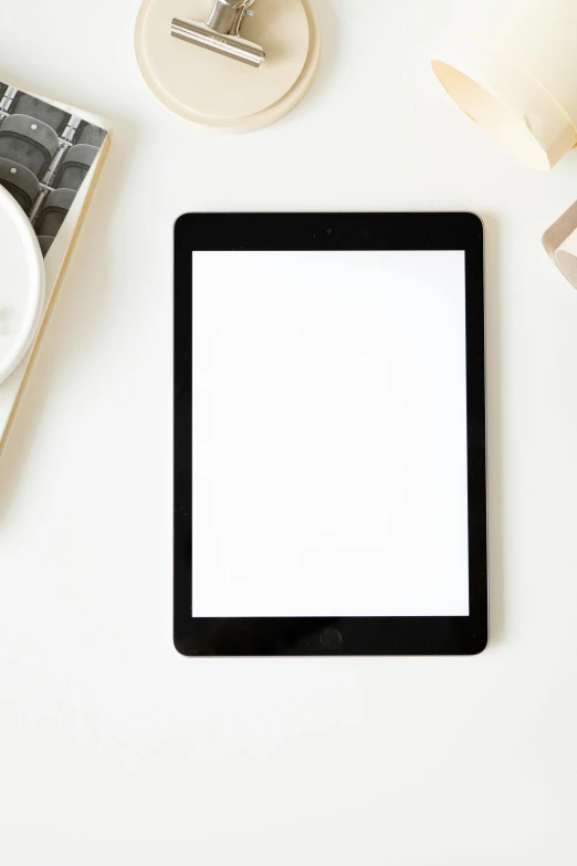 a tablet computer sitting on top of a desk next to a cup of coffee, white space, square, uploaded, item