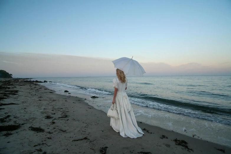 a woman standing on a beach holding an umbrella, an album cover, inspired by Wilhelm Hammershøi, romanticism, white regal gown, promo photo, evening at dusk, white