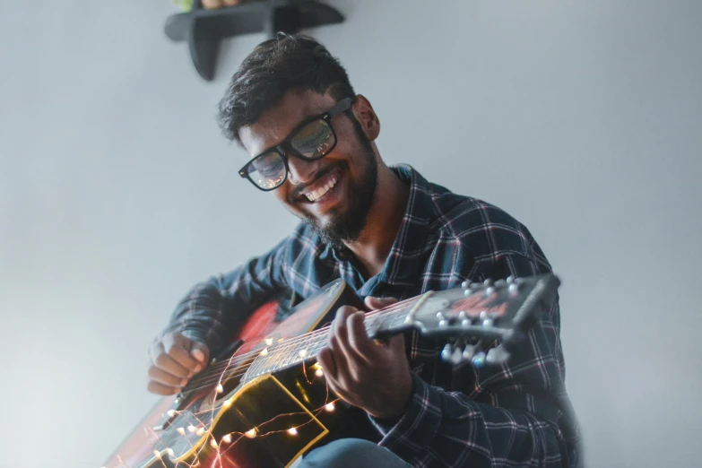 a man sitting on a bed playing a guitar, inspired by Michael Ray Charles, pexels contest winner, hurufiyya, with glasses on, avatar image, beautiful and smiling, lights on