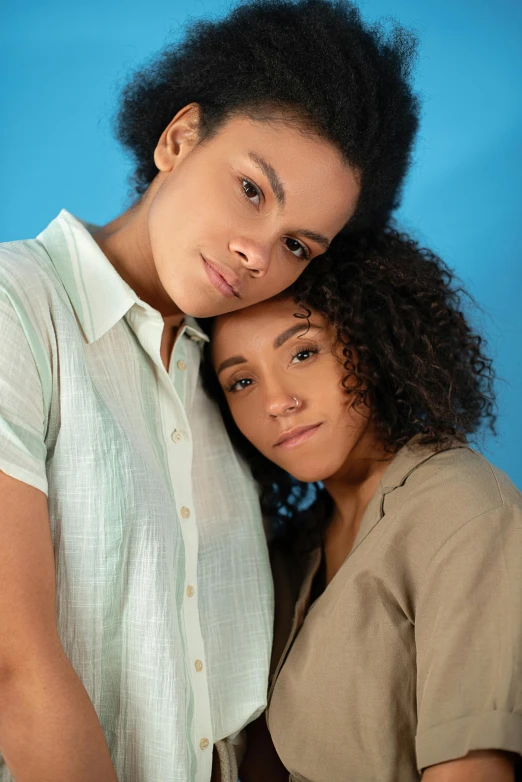 a couple of women standing next to each other, trending on pexels, renaissance, light-brown skin, wearing a light blue shirt, lesbian embrace, brown curly hair