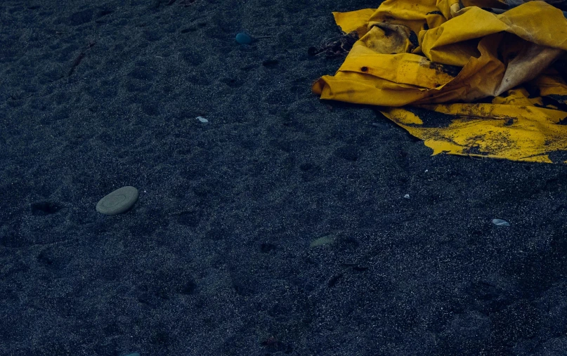 a yellow blanket sitting on top of a sandy beach, a picture, unsplash, plasticien, moonlight showing injuries, garbage, yellow clothes, blue sand