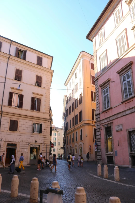 a group of people walking down a street next to tall buildings, inspired by Romano Vio, renaissance, pink marble building, prefecture streets, far away from camera, stacked houses