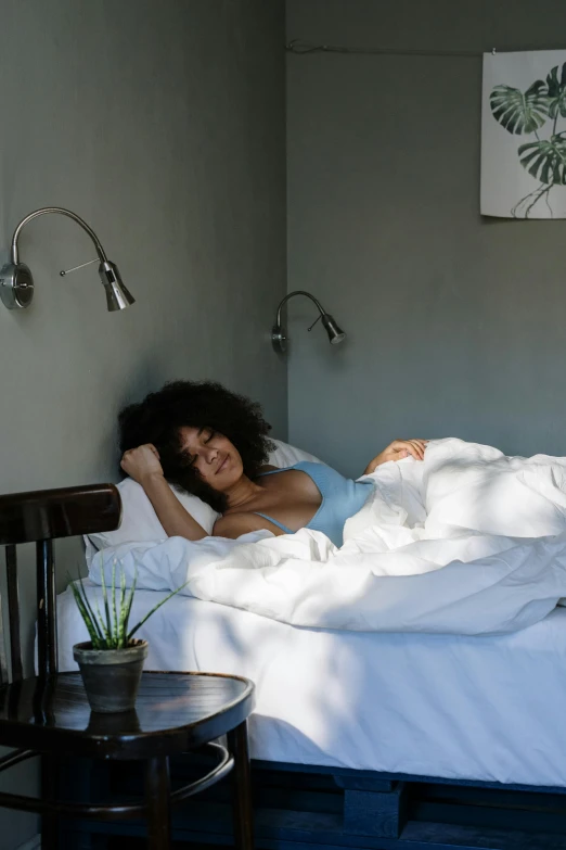 a woman laying on top of a bed in a bedroom, premium quality, lights off, natural light outside, grey