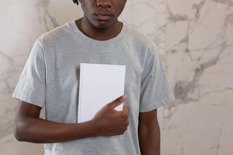 a young man holding a piece of paper in his hand, an album cover, inspired by Xanthus Russell Smith, pexels contest winner, private press, plain white tshirt, holding notebook, the book is closed, with grey skin