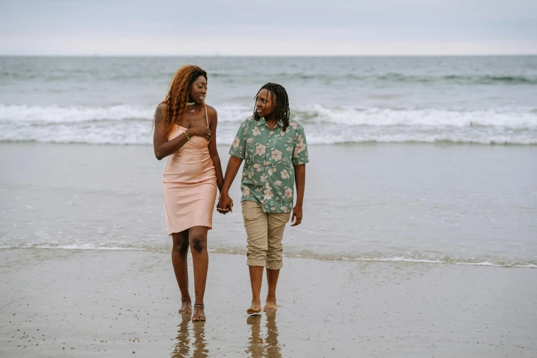 a man and a woman walking on a beach, a portrait, by Carey Morris, pexels, lesbian, with brown skin, 2 people, breeding