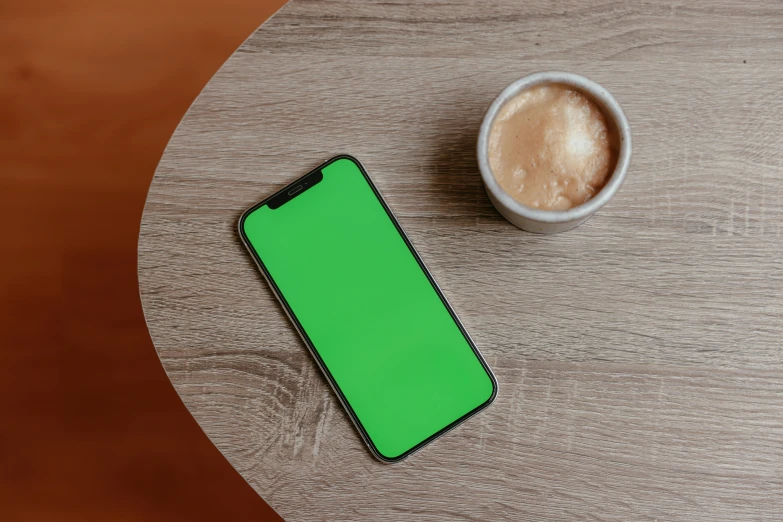 a cell phone sitting on top of a wooden table next to a cup of coffee, by Andries Stock, trending on pexels, color field, green screen, hyper realistic 3 d render, gradient green black, no - text no - logo