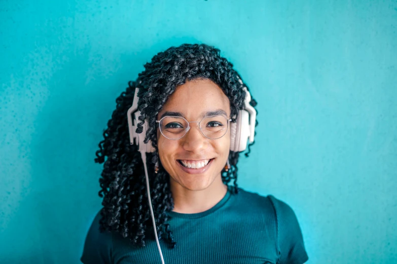 a close up of a person wearing headphones, pexels contest winner, antipodeans, dark short curly hair smiling, relaxed. blue background, wavy long black hair and glasses, mixed race