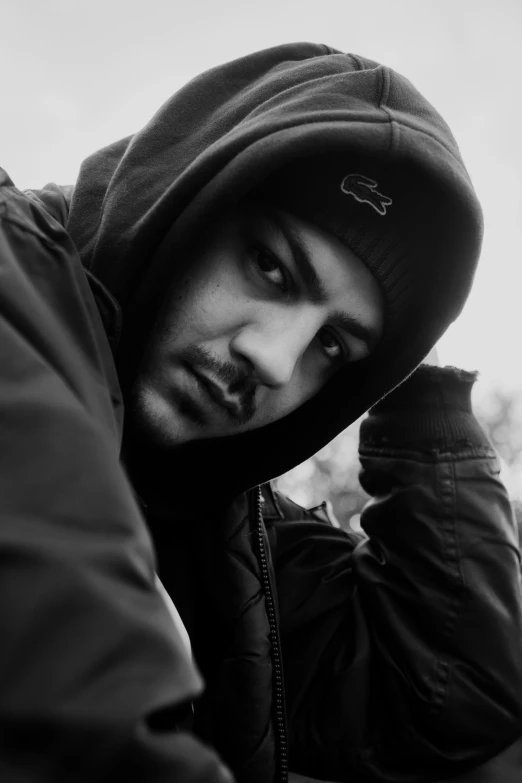 a black and white photo of a man in a hoodie, by Altichiero, grime, kyza saleem, a man wearing a black jacket, in a chill position