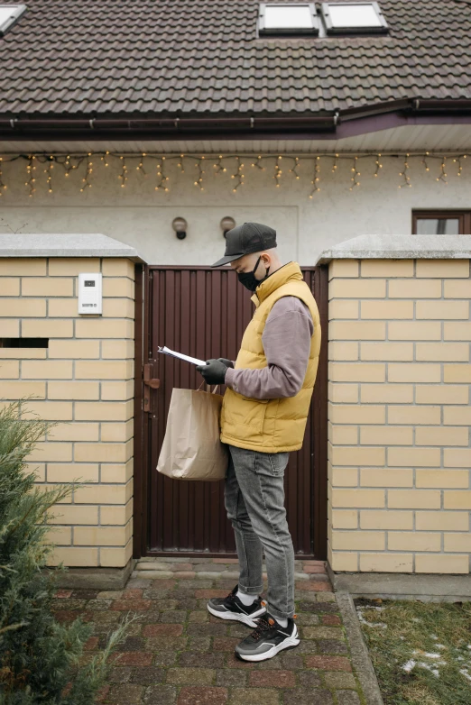 a man in a yellow vest standing in front of a house, pexels contest winner, private press, delivering mail, brown, inspect in inventory image, man wearing a closed cowl