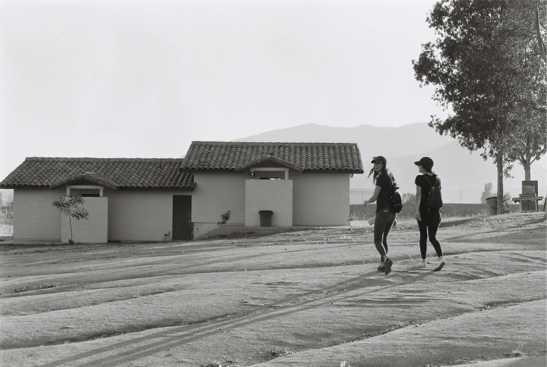 a couple of people that are standing in the dirt, a black and white photo, inspired by Dorothea Lange, unsplash, renaissance, hearst castle, huts, walking on the street, medium format. soft light