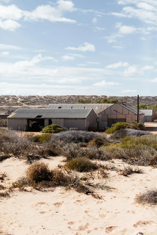 a man riding a skateboard on top of a sandy beach, by Lee Loughridge, trending on unsplash, modernism, wide view of a farm, shed, rocky desert, old lumber mill remains