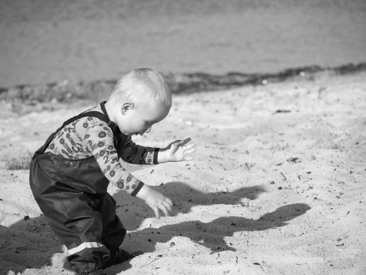 a black and white photo of a toddler playing in the sand, a black and white photo, pexels, small man, performance, future tech, seaside