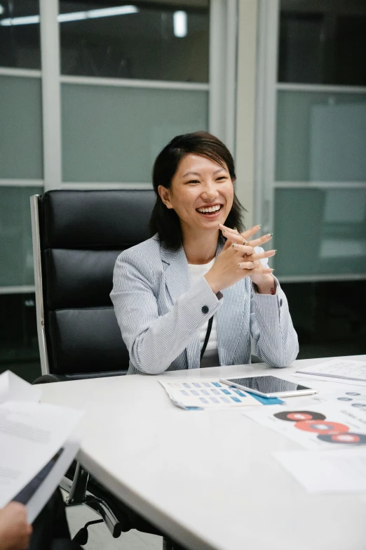 a woman sitting at a table with papers in front of her, by Jang Seung-eop, laughing, ceo, with index finger, in office