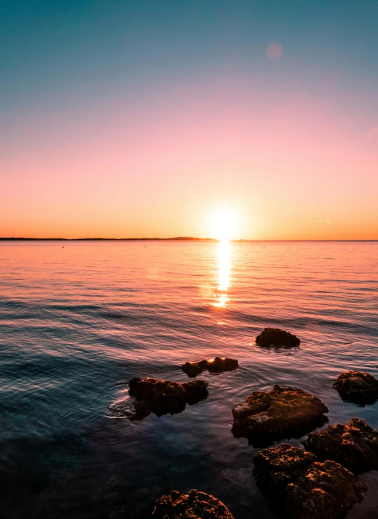 a sunset over a body of water with rocks in the foreground, a picture, croatian coastline, stunning screensaver, visually crisp & clear, ultrawide landscape