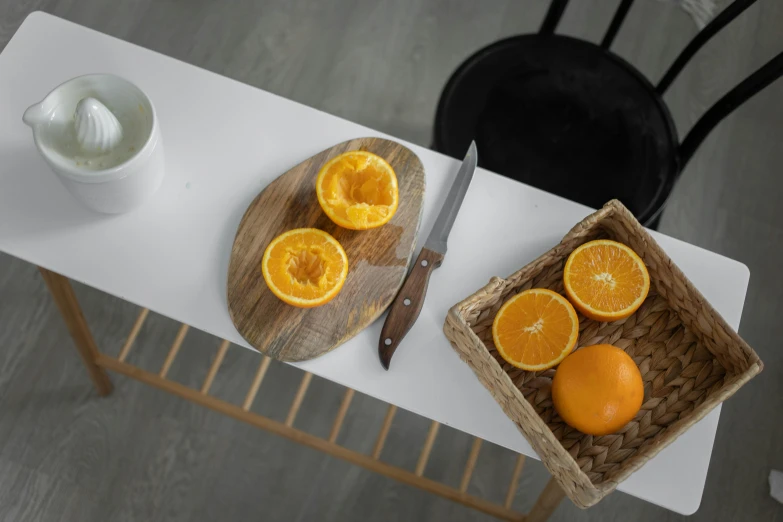 a bowl of oranges and a knife on a table, inspired by Constantin Hansen, pexels contest winner, wooden coffee table, orange grey white, kitchen counter, set against a white background