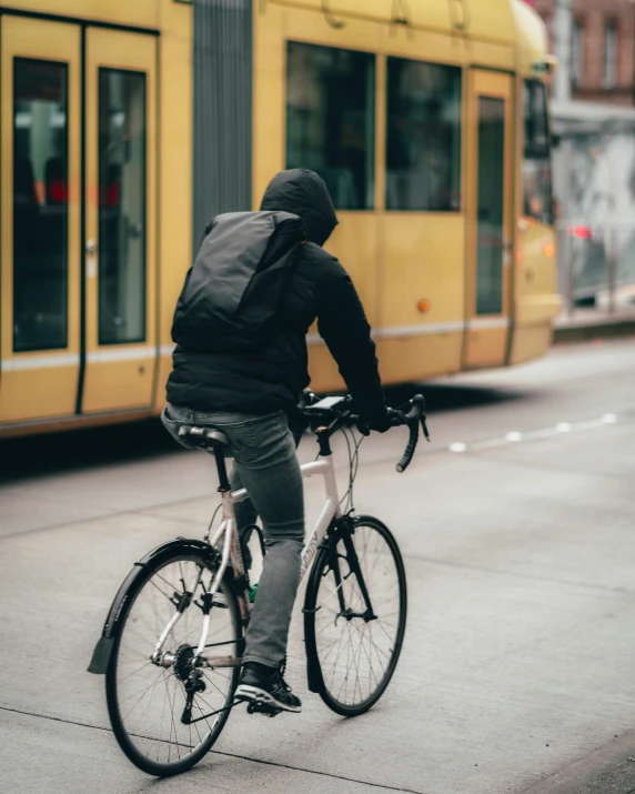 a person riding a bike on a city street, hat and hoodie, with a backpack, profile image, back facing