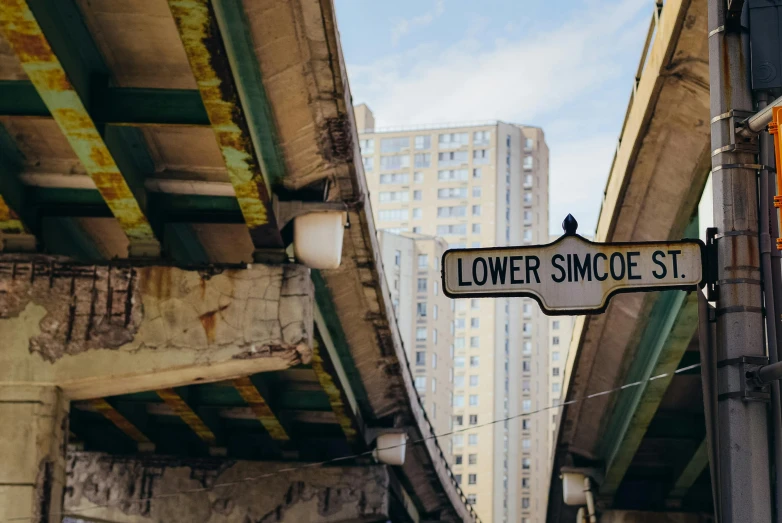 a street sign hanging from the side of a bridge, inspired by Sidney Simon, pexels contest winner, annie lebowitz, lower and upper levels, chicago, slimmer demeanor