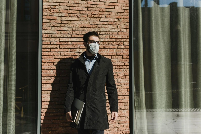 a man standing in front of a brick building, facemask, sunday afternoon, trench coat, intelligence