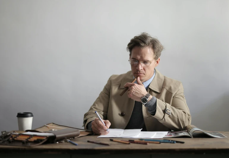 a man sitting at a table with a pen and paper, inspired by Christoffer Wilhelm Eckersberg, pexels, academic art, gary oldman as a pear, wearing reading glasses, hugh grant, profile image