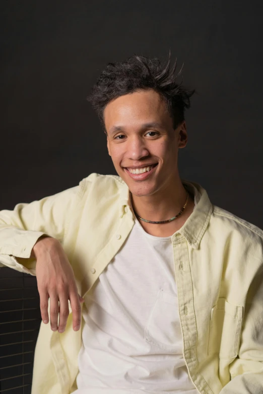 a man in a yellow shirt posing for a picture, inspired by Reuben Tam, in front of a black background, androgynous male, aged 2 5, smiling male